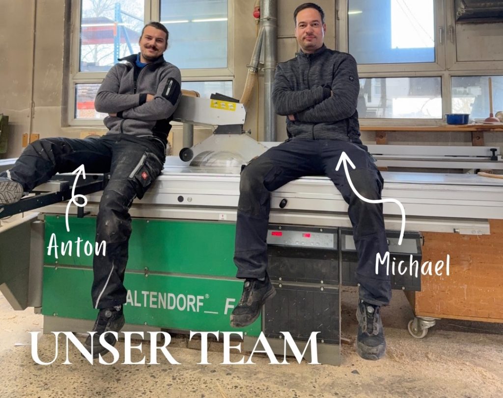 Anton und Michael sitzen Seite an Seite auf einer Altendorf-Formatkreissäge in der Werkstatt – entspannt, mit verschränkten Armen.