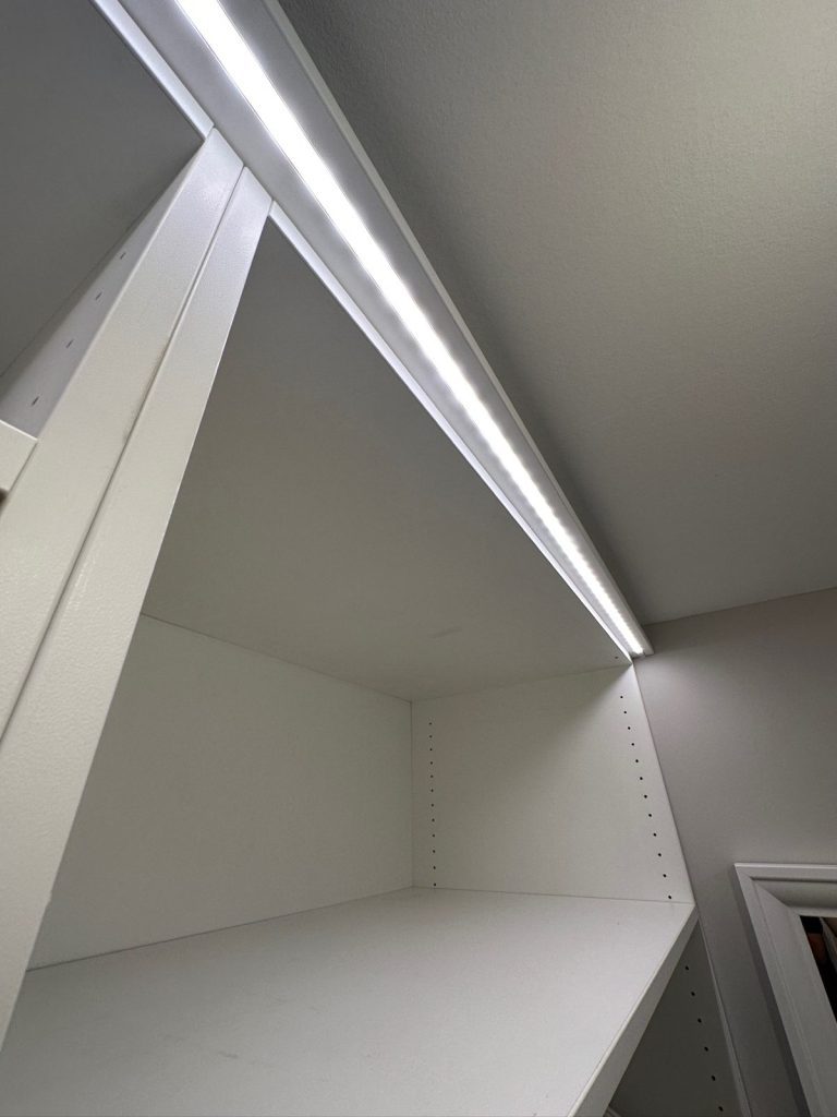 Integrierte LED-Lichtleiste an der Oberkante eines weißen Einbauregals nach Maß – indirekte Schrankbeleuchtung in der Ankleide