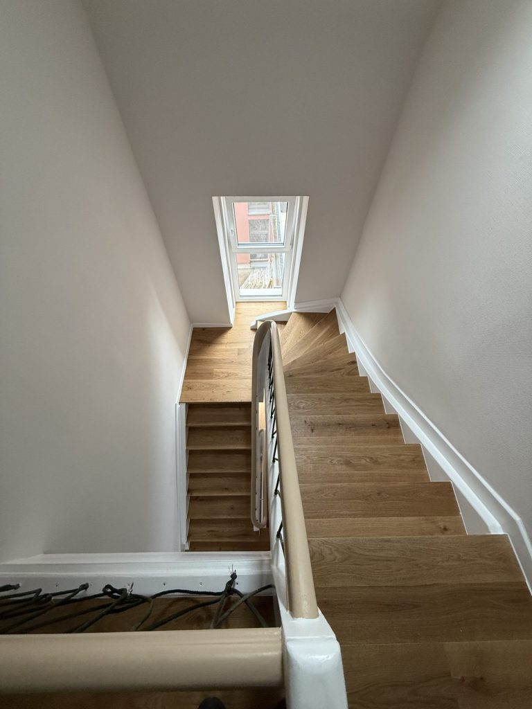 Blick ins Treppenhaus: sanierte Treppe mit Trittstufen aus Eiche-Parkett, Podest und weißen Wangen – Schreinerei Holzmanufaktur Wilhelm
